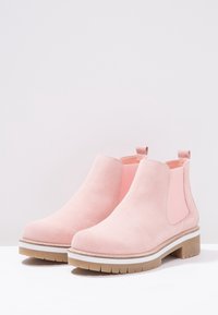 Różowe zamszowe botki za kostkę z elastycznymi panelami bocznymi i pętlami do zakupu, z masywną gumową podeszwą, białą akcentującą linią i okrągłym noskiem.