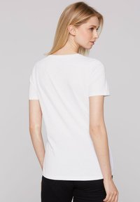 Biała koszulka z krótkim rękawem wykonana z bawełny. Klasyczny krój z okrągłym dekoltem, gładka faktura oraz prosty design bez ozdób.