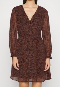 Brun och svart zebra-mönstrad omlottklänning i lätt, genomskinlig tyg med långa ärmar och djup V-ringning, åtdragen vid midjan.