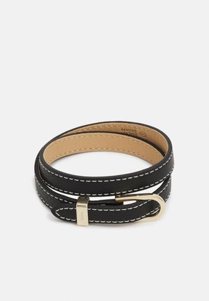 Zwarte armband van echt leer met witte stiksels en gouden gesp, opgerold in een cirkelvorm op een witte achtergrond.