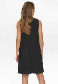 Vestido negro sin mangas, de longitud a la rodilla, con tejido suave, con una silueta recta y sutiles detalles en la costura trasera.