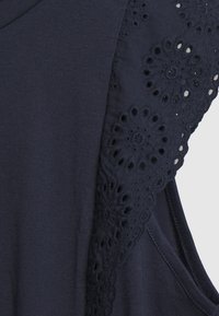 Navy blue tank top, jossa on kukkakuvioinen pitsi yhdellä olkaimella, tehty pehmeästä puuvillasta, joka tuntuu sileältä ja on rento istuvuus.