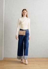 Slonovinová blúzka s dlhým rukávom a skrúteným dizajnom, kombinovaná s tmavými širokými nohavicami so svetlými manžetami a ružovou crossbody taškou.