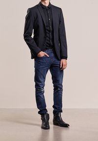 Black blazer over a black button-up shirt, paired with distressed blue jeans and black ankle boots. Smooth fabric, tailored fit.