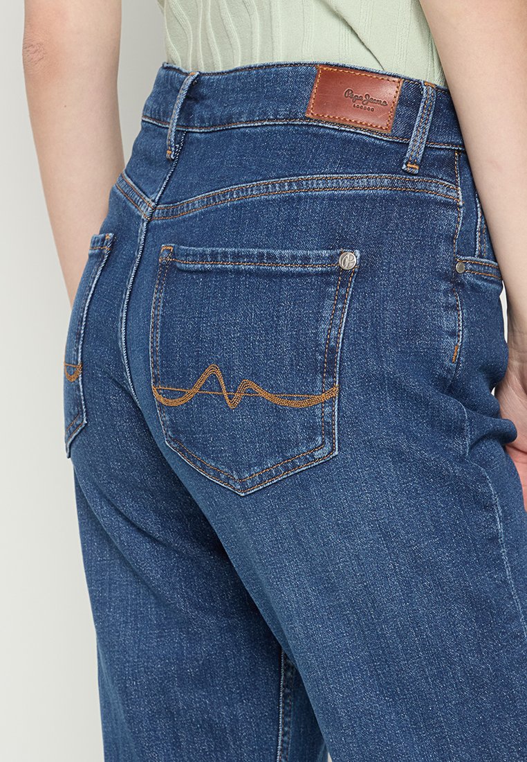 Dunkelblaue Denim-Jeans mit einem Leder-Logo-Patch, zwei Gesäßtaschen mit orangefarbenem Zickzack-Stich und einer taillierten Passform.