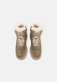Bottes en daim vert avec un revers en fausse fourrure blanche, dotées de lacets beiges et d'un design à bout arrondi, reposant sur une semelle de couleur claire.