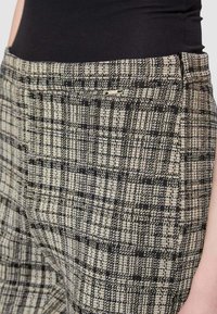 Pantaloni a quadri in bianco e nero con tessuto testurizzato, caratterizzati da un piccolo dettaglio metallico vicino alla vita e da un design aderente.