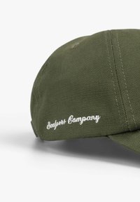 Gorra verde hecha de tela texturizada, con el texto bordado en blanco "Sayless Company" en el panel frontal. Visera curvada y detalles cosidos.