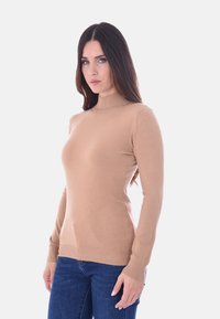 Maglione a maniche lunghe color tan con collo alto, realizzato in un tessuto morbido e liscio, con polsini e orlo a coste, abbinato a jeans blu scuro.