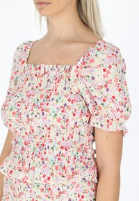 Bluse mit Blumenmuster, kurzen Puffärmeln, quadratischem Ausschnitt und geraffter Textur in Pastellfarben. Sie hat einen rüschenbesetzten Saum und elastische Bänder.
