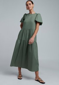 Roheline, põlveni ulatuv kleit tekstuurse kangaga. Omab tuftükkidega varrukaid ja kihilist ääreosa. Sobitatud mustade sandaalidega.