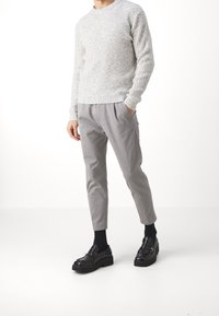 Jasnoszary sweter z prążkowanej dzianiny w połączeniu z jasnoszarymi, taliowanymi spodniami; czarne mokasyny z grubą podeszwą; gładka tekstura, elegancki design.
