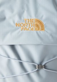 Ανοιχτό μπλε ύφασμα με το χρυσό κεντημένο λογότυπο "The North Face" και ένα γκρι ρυθμιζόμενο σύστημα κλειδώματος με κορδόνι.