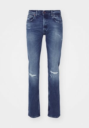 Tmavě modré džíny z denimu se rovnými nohavicemi, opotřebovanými záplatami na kolenou, pěti kapsami a zapínáním na knoflík v pase.