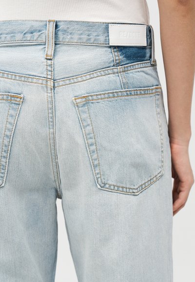 Φωτεινά μπλε τζιν που φοριούνται από άτομο, που εμφανίζουν πίσω τσέπες, θηλιές για ζώνη και μια λευκή ετικέτα στη μέση.