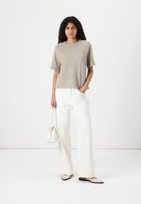 Beige short-sleeve top, relaxed fit; paired with white wide-leg pants. Accessories include a small white handbag and light-colored slip-on shoes.