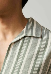 Kurzarmhemd mit einem gestreiften Muster in Grün und Creme, das eine weiche Textur und ein klassisches Kragendesign aufweist.