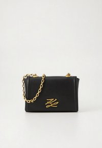 Černá obdélníková kožená kabelka se zlatým řetízkovým řemínkem a zlatým stylizovaným logem "K" na přední straně, na jednobarevném bílém pozadí.