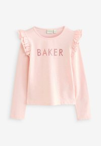 Gaiši rozā krekls ar gariem piedurknēm un ruffled akcentiem uz pleciem, uz kura priekšpuses ir vārds "BAKER" spīdīgos burtos.