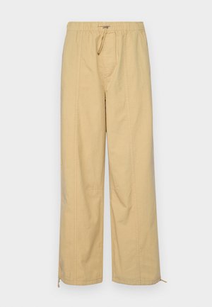 Beige wide-leg pants with an elastic waistband, drawstring detail, and zippers at the ankles. Smooth texture with subtle vertical lines.