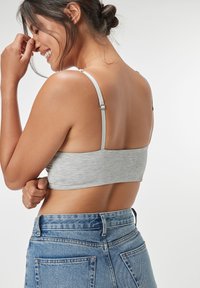 Grå kort topp i mjukt tyg med tunna justerbara band. Buren med högmidjade blå denimjeans med bakfickor.