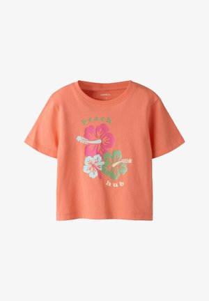 T-shirt corallo a maniche corte con tre fiori di ibisco in rosa, bianco e verde, con la scritta "beach hub" sopra e sotto i fiori.