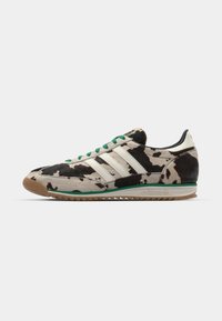 Adidas sneakers with cowhide-patterned upper, green laces, three white stripes, and a brown rubber sole. Rounded toe design.