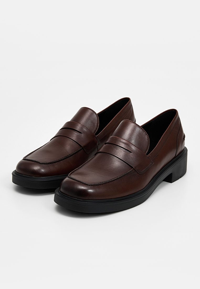 Mocassins en cuir brun avec un design confortable, présentant un bout cousu, un détail de sangle et un petit talon en caoutchouc noir.