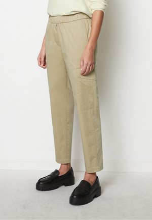 Pantalons cargo beiges avec une taille élastique, des poches latérales, une coupe ample et un tissu lisse et léger. Associés à des chaussures noires à enfiler.