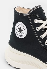 Baskets montantes en toile noire avec des coutures blanches, dotées d'un écusson logo circulaire et d'une semelle épaisse couleur crème.