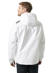 Chaqueta impermeable blanca con capucha, que presenta un logo negro en el hombro, textura suave y un corte holgado.