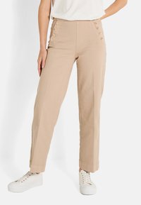 Pantalones beige de cintura alta con botones laterales, perneras rectas y una textura suave. Combinados con zapatillas blancas para un look casual.