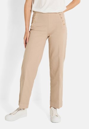 Pantalons beiges taille haute avec boutons sur les côtés, jambes droites et texture lisse. Associés à des baskets blanches pour un look décontracté.