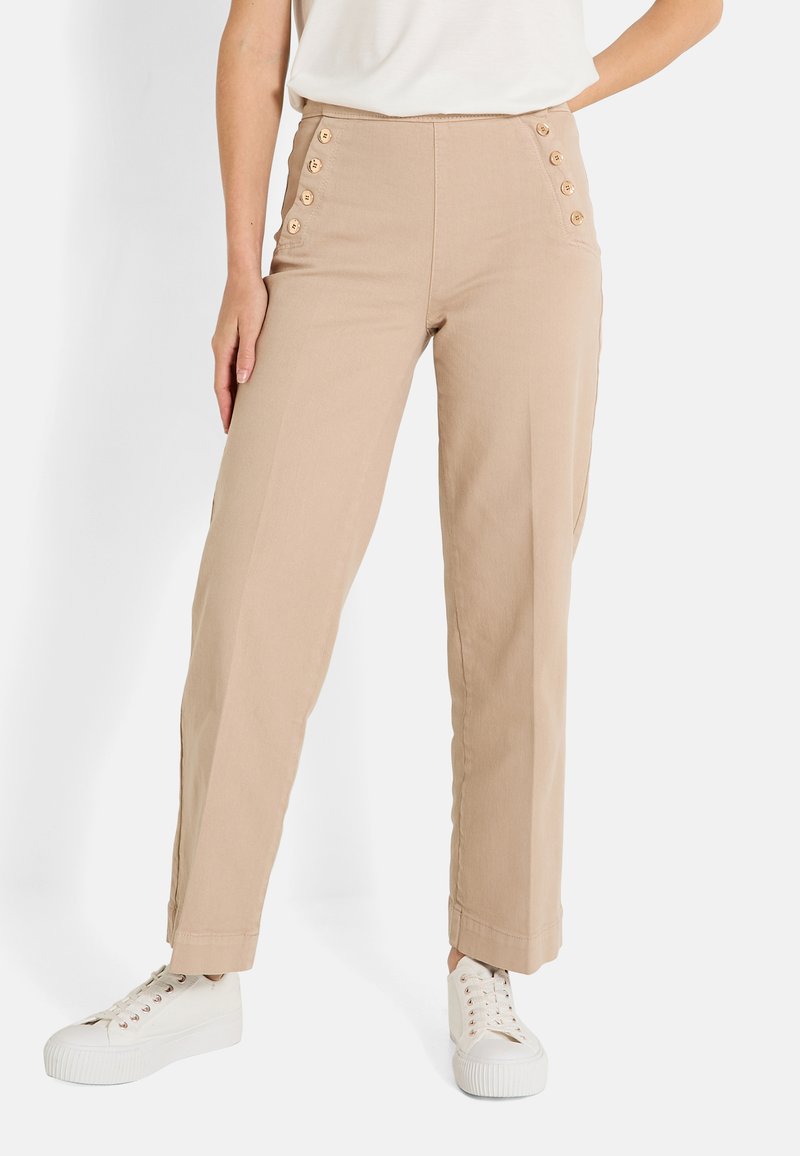 Pantalones beige de cintura alta con botones laterales, perneras rectas y una textura suave. Combinados con zapatillas blancas para un look casual.