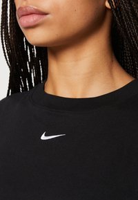 Czarny bawełniany sweatshirt z okrągłym dekoltem, z małym białym logo Nike na piersi. Tekstura wydaje się gładka i miękka.