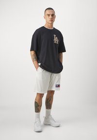 Camiseta negra de corte oversized con logo de LA y cuello blanco. Pantalones cortos de malla blancos con logo de Champion. Zapatillas blancas y calcetines de diseño.