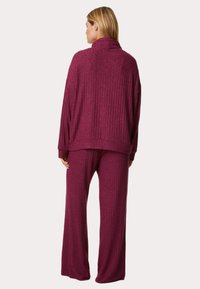 Burgundy two-piece outfit featuring a ribbed texture, oversized sweater with a high neck, and wide-leg pants for a relaxed fit.