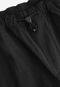Schwarzer elastischer Bund mit verstellbarem Kordelzug. Leichter Stoff mit subtiler Textur. Glatte Oberfläche, minimalistisches Design.