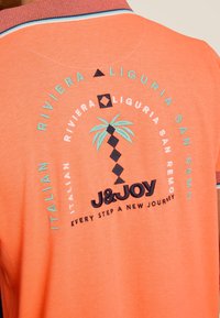 Koraalrode polo shirt met een contrasterende kraag, geborduurd logo en print van een palmboom en tekst, gemaakt van een textuurstof.