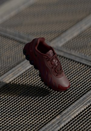 Maroon athletic shoe with a textured upper, prominent laces, and visible air cushioning pods. Features sleek lines and a glossy toe cap.