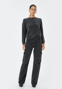 Maglione grigio a coste con maniche lunghe, abbinato a pantaloni cargo neri a vita alta con ampi tasche laterali e una vestibilità rilassata.