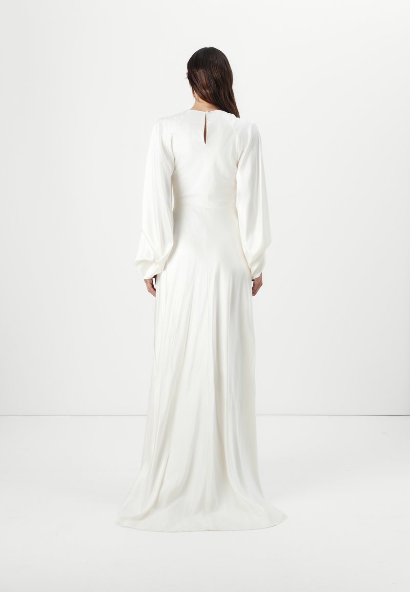 Robe longue blanche avec des manches bouffantes, texture satin lisse, détail en keyhole au dos et jupe fluide. Design simple et élégant.