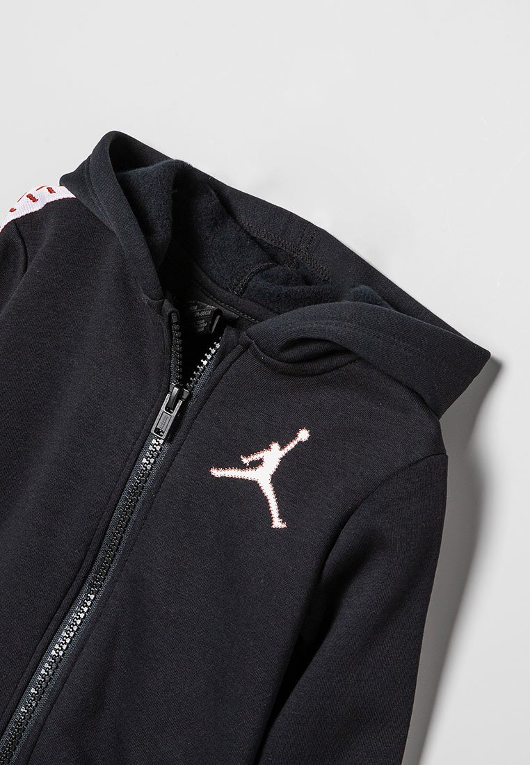 Felpa nera con zip realizzata in pile, presenta un logo Jumpman rosa sul petto e strisce bianche a contrasto sulle spalle.