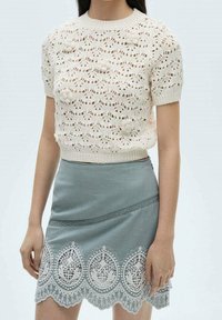 Haut à manches courtes en tricot avec un tissu crème texturé présentant un motif ondulé et des détails floraux. Associé à une jupe bleu clair avec une bordure en dentelle.