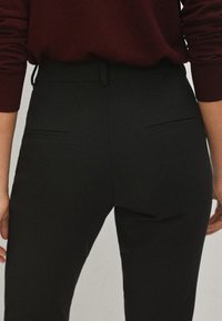 Pantalons noirs en tissu lisse, avec une taille haute et deux poches arrière. Le design est ajusté avec une coupe droite.