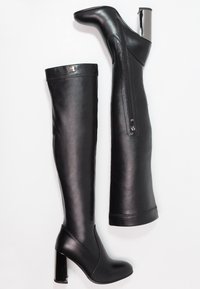 Botas altas de muslo negras con tacones, hechas de cuero suave, que cuentan con una cremallera frontal y un tacón cuadrado brillante. Costuras visibles en la parte superior.