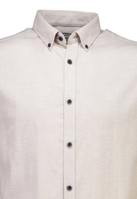 Camicia beige con bottoni neri e colletto bottonato, mostrata dalla vita in su su uno sfondo bianco.