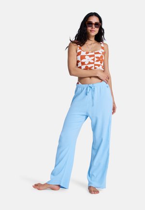 Haut court à fleurs blanches et orange associé à un pantalon bleu clair, coupe décontractée. Le tissu est doux au toucher, avec une taille ajustable par cordon sur le pantalon.