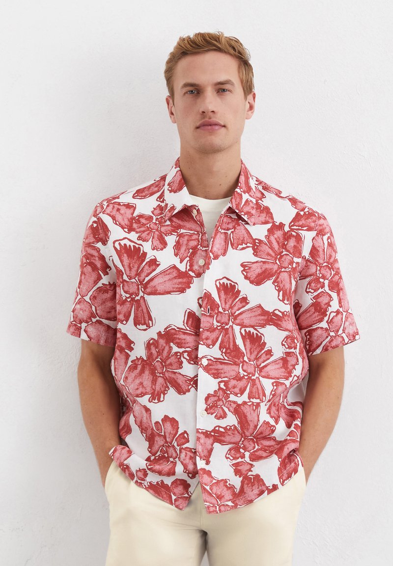 Korte mouwen shirt van witte stof met een rood bloemenpatroon. Heeft een puntige kraag en knoopsluiting aan de voorkant. Gladde textuur, ontspannen pasvorm.