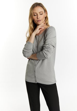 Cardigan grigio con bottoni, maniche lunghe, polsini a costine e una texture morbida. Indossato sopra pantaloni neri, presenta un design dalla vestibilità ampia.